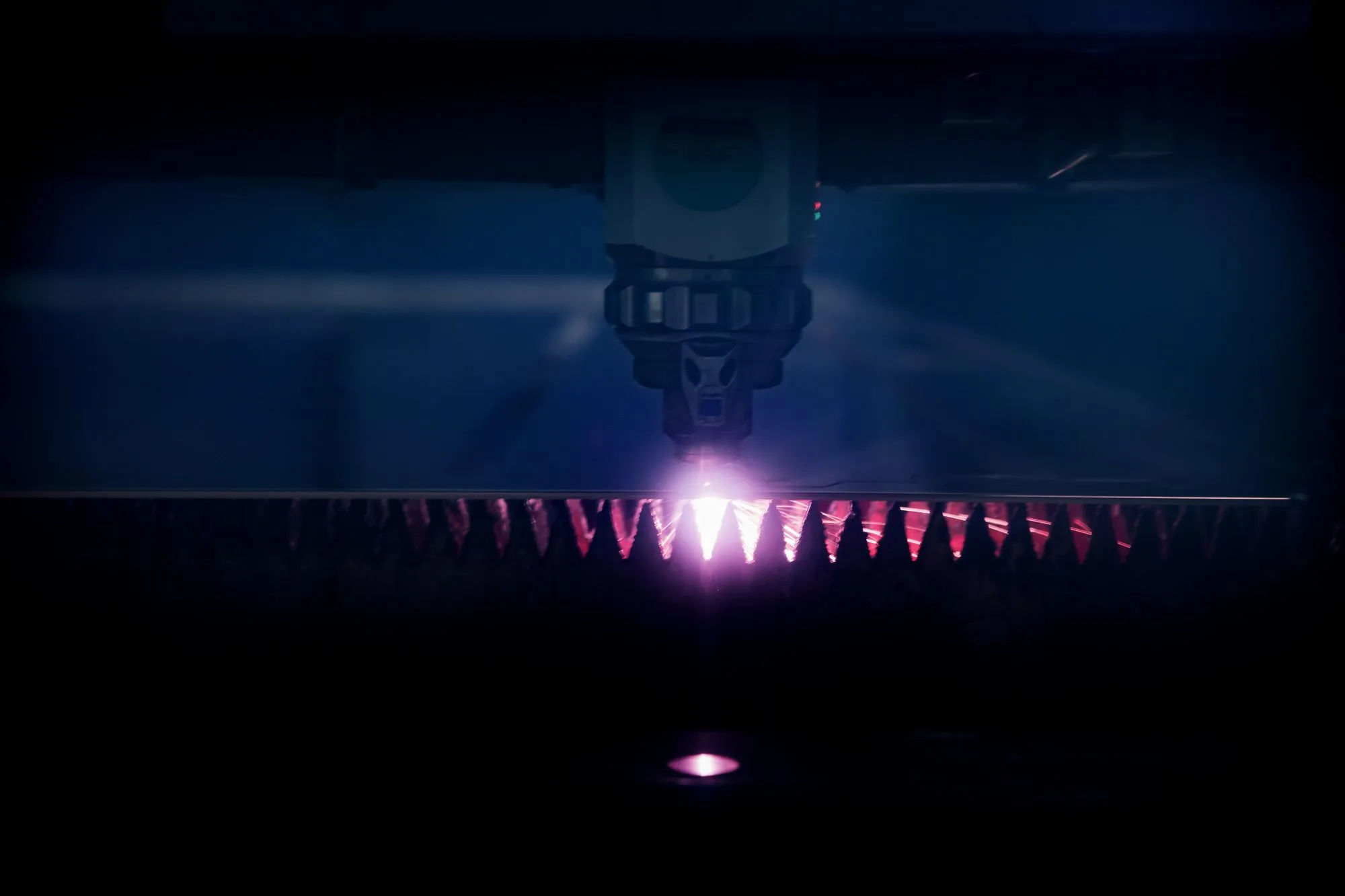 Snijkop van de lasersnijmachine boven de plaat, met een rij vonken langs de snede