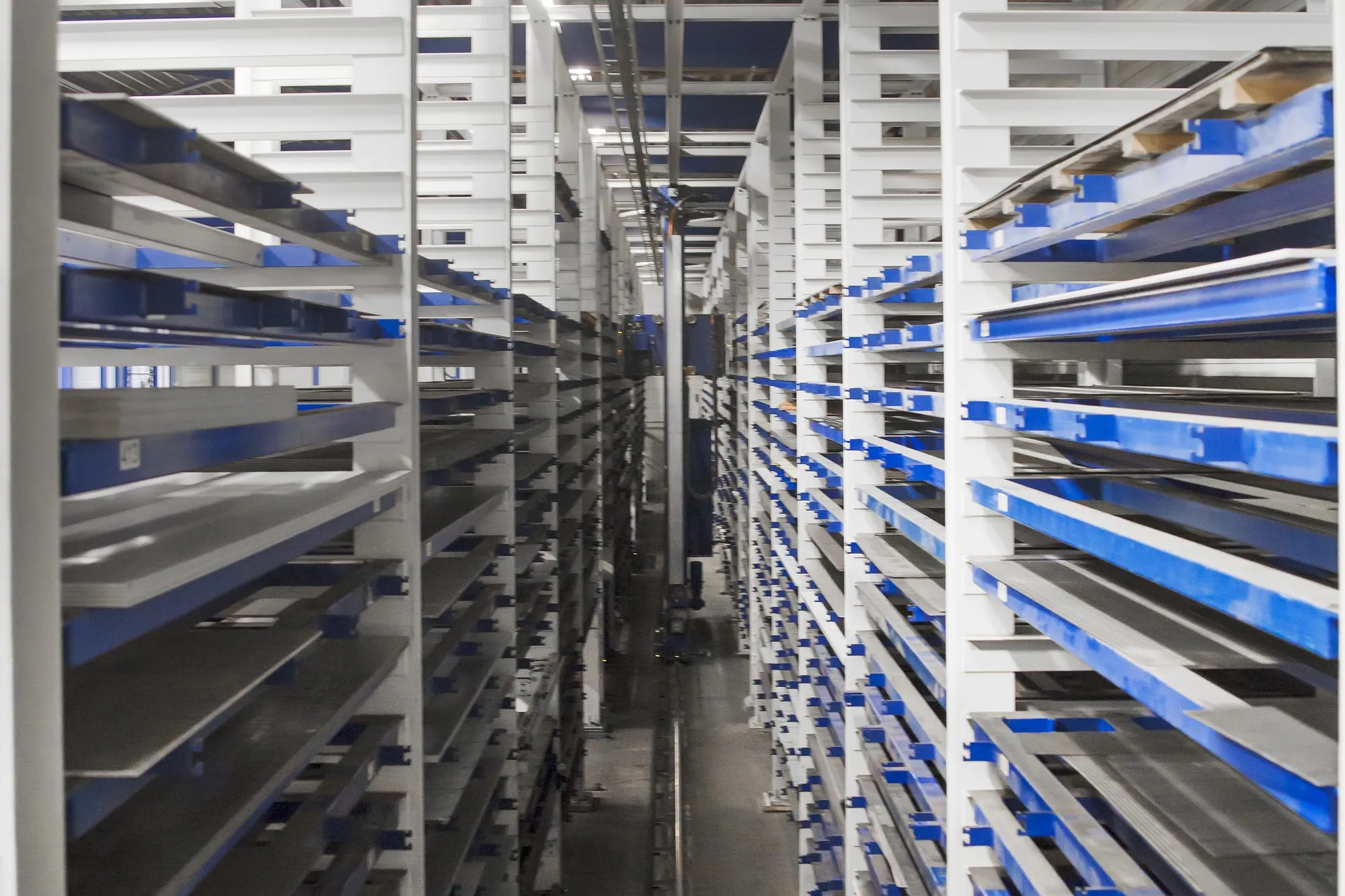 Gang tussen de torens van het plaatmagazijn, met plaatmateriaal op blauwe laden
