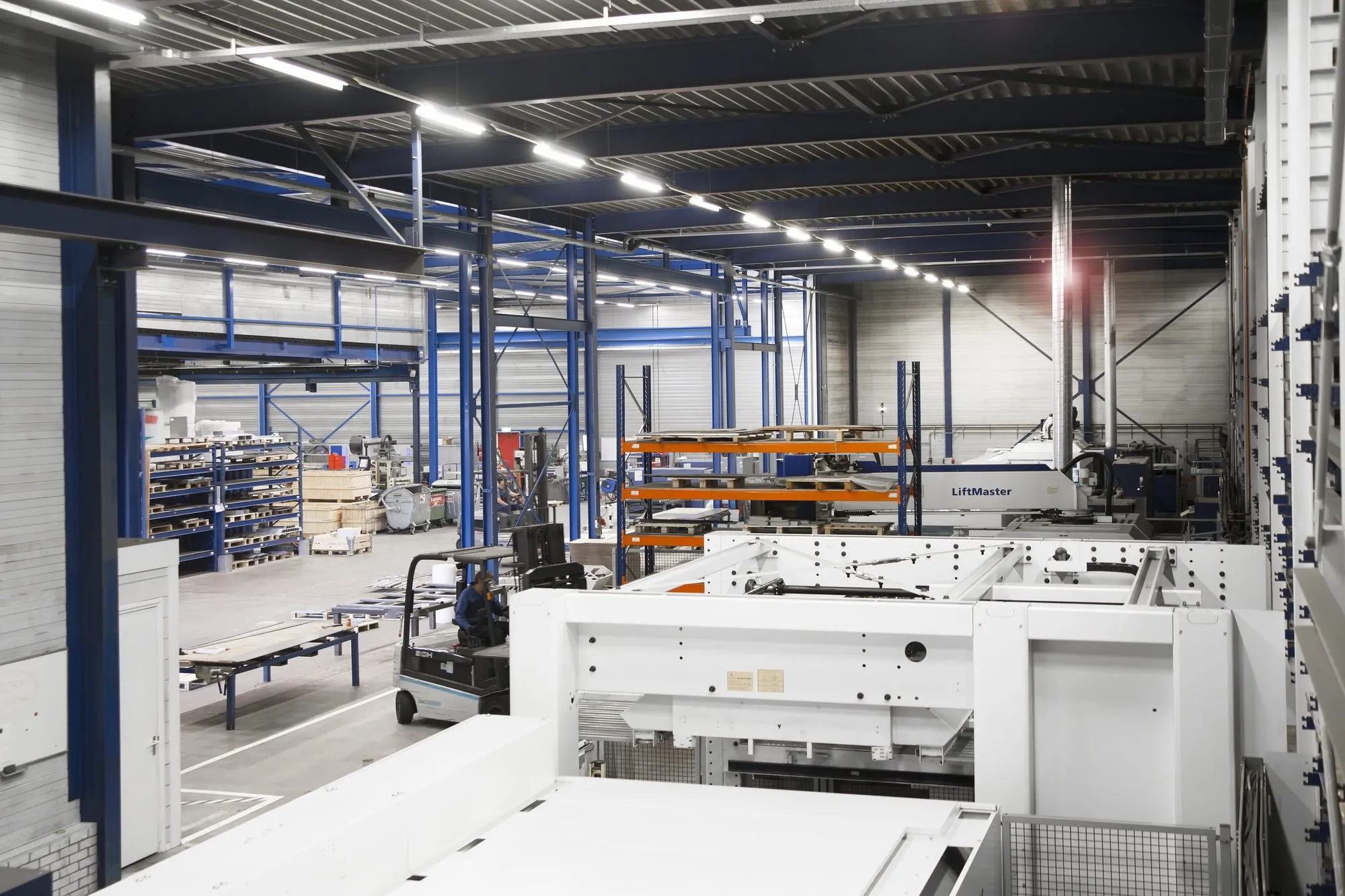 Productiehal met een lasersnijmachine en het automatische laadsysteem, met stellingen en een heftruck op de achtergrond
