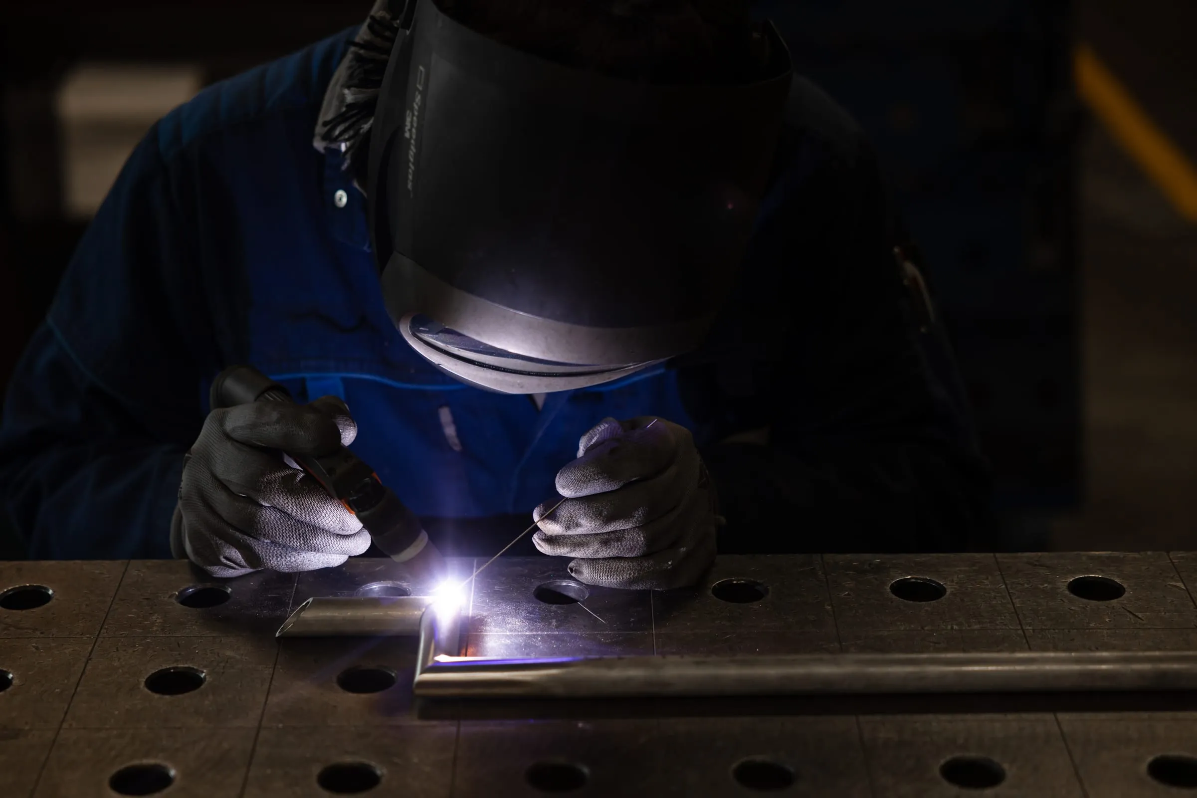 Lasser werkt met de hand aan een klein onderdeel op de lastafel